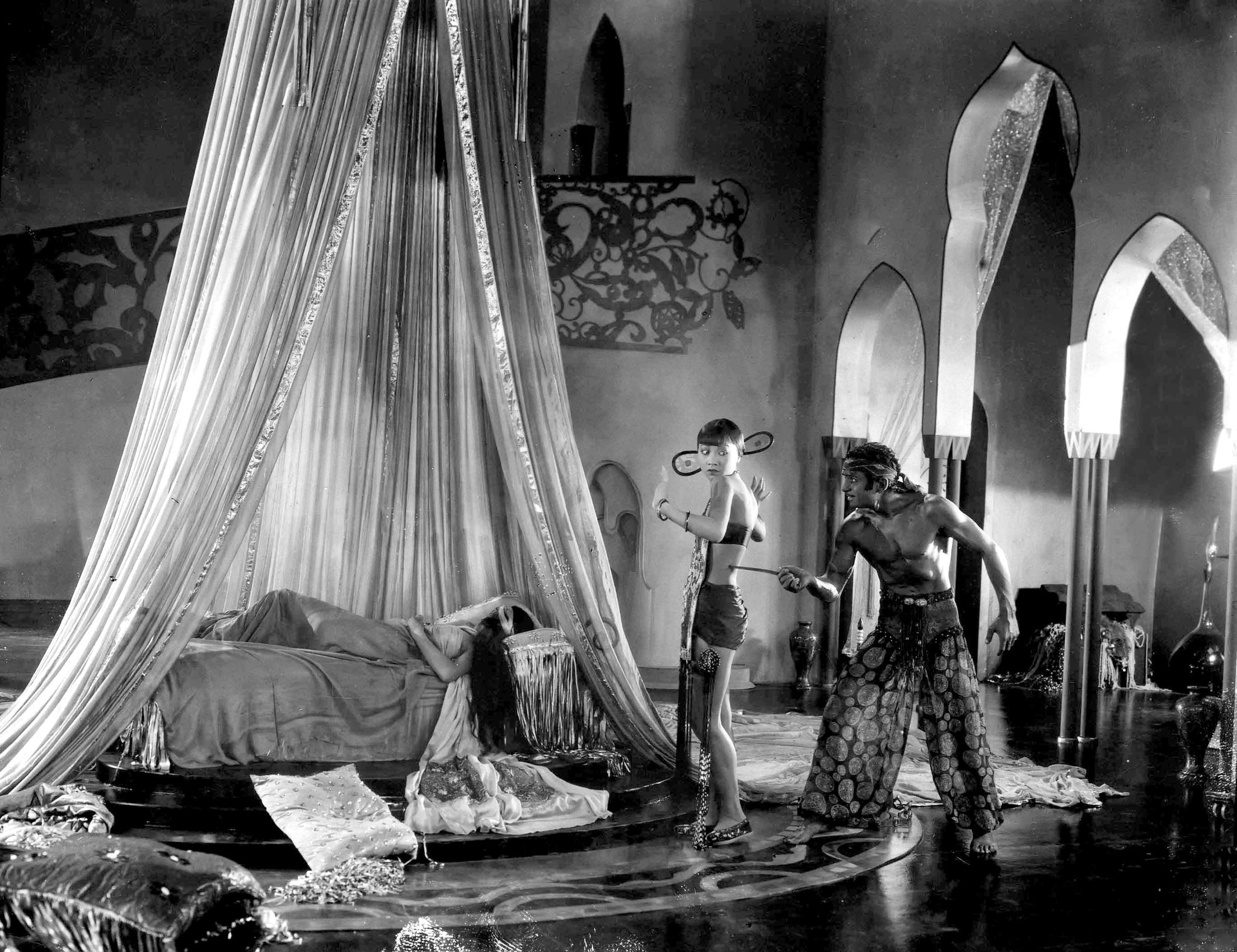 Douglas Fairbanks as Ahmed, the Thief of Bagdad threatening Anna May Wong as the Mongol Slave with Julanne Johnston as The Princess sleeping 1924 The Thief of Bagdad picture image